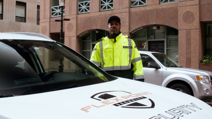 A male Flex Point Security guard standing next to a company vehicle in Downtown, Toronto