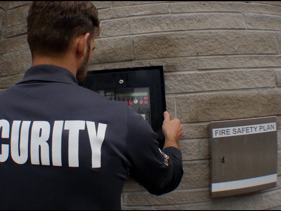A licensed Flex Point Security guard inspecting a fire alarm panel outside of a building