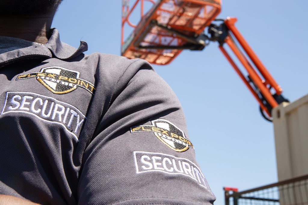 Close up of a Flex Point Security guard's arm and chest with a crane in the background at a logistics site