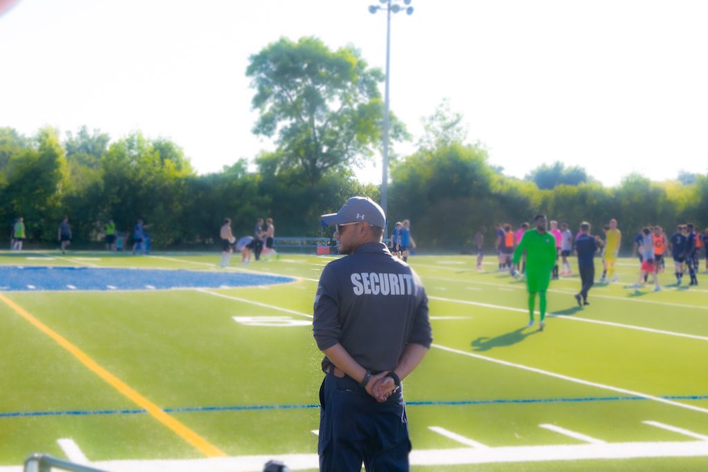 A Flex Point Security guard standing on the sidelines of a soccer field with players on the field