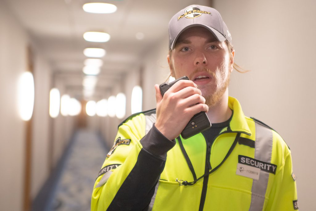 Flex Point Security guard walking down a residential building's hallway speaking on a walkie talkie with co-worker