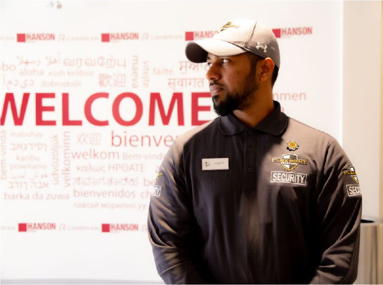 A Flex Point Security guard standing in front of a large sign that says the word "welcome" in many languages