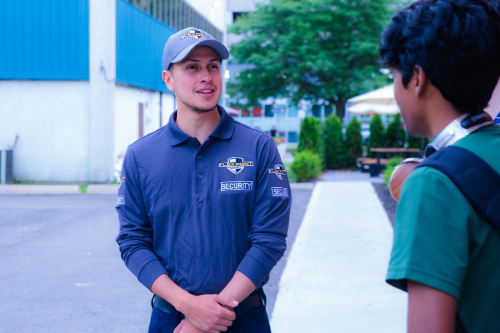 A licensed Flex Point Security guard in full uniform standing and speaking with a student in an outdoor setting