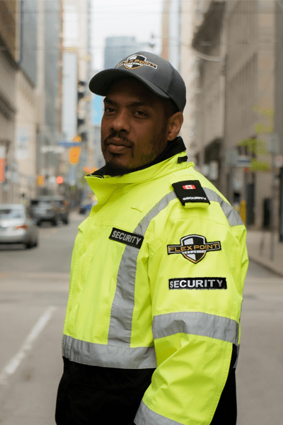 Flex Point Security guard standing at a Toronto intersection with a bright yellow branded jacket and grey branded hat
