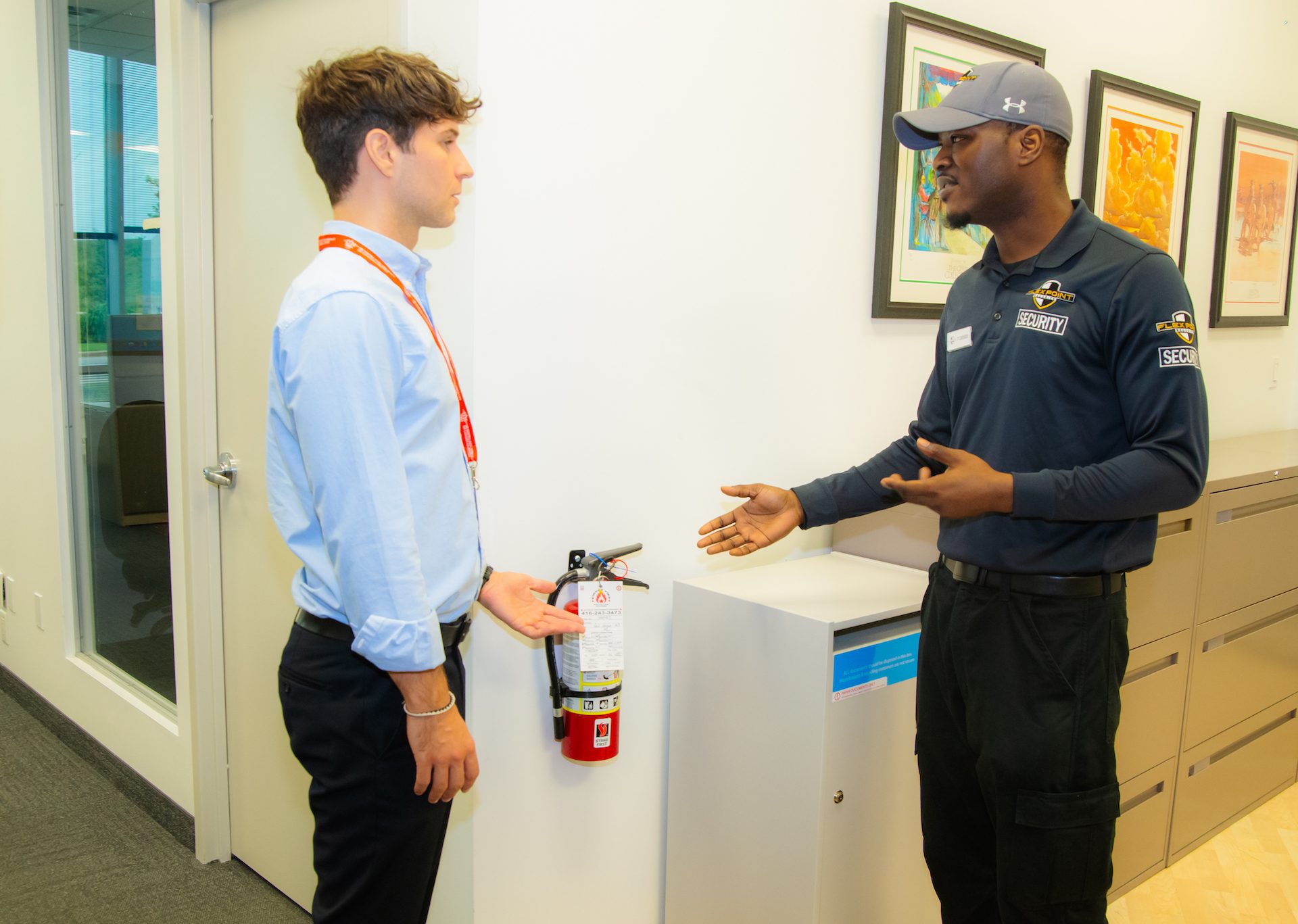A male Flex Point Security guard speaking with a male employee at an office about fire prevention next to a fire extinguisher