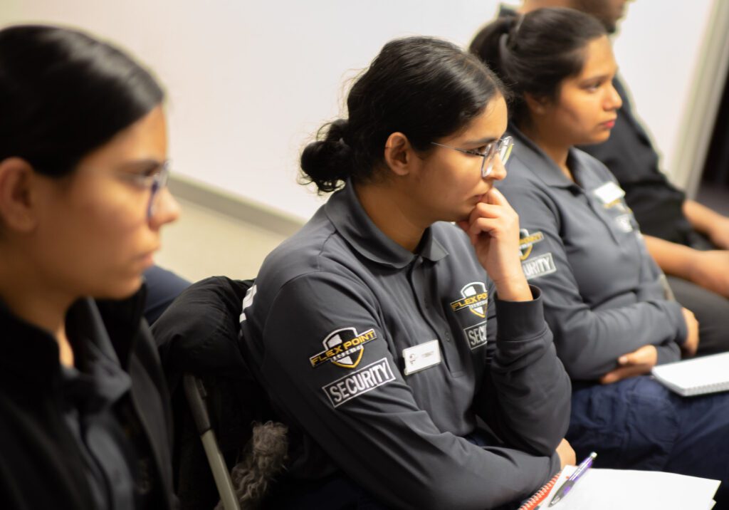 Three female security guard training trainees sitting and listening to an instructor teach the course