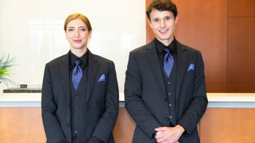 A male and female Flex Point Security concierge guards in formal attire standing together in front of a concierge desk