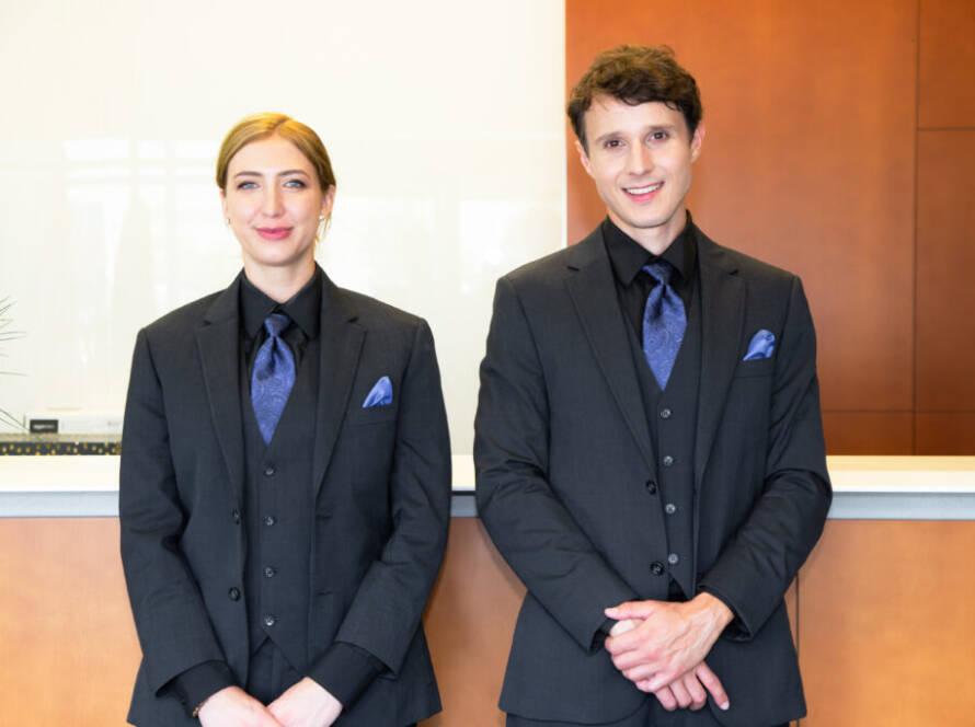 A male and female Flex Point Security concierge guards in formal attire standing together in front of a concierge desk