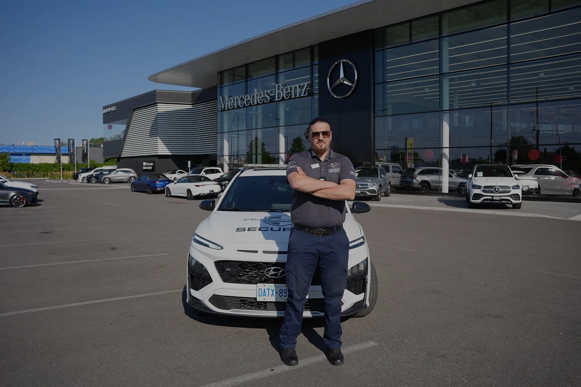 A male Flex Point Security guard standing in front of a company branded vehicle while on-site at a Mercedes-Benz dealership in the Greater Toronto Area