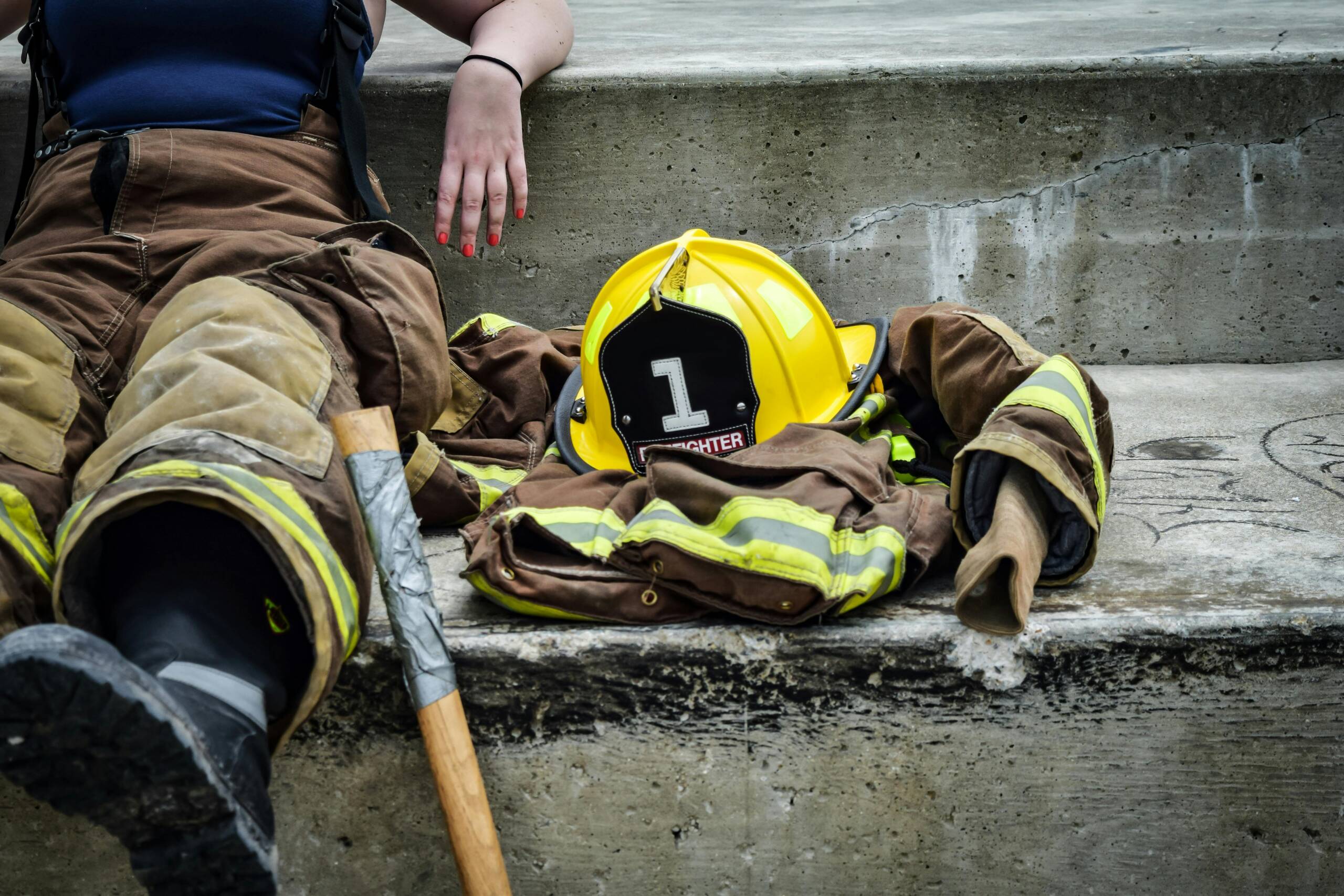 A female firefighter sitting on the concrete steps with some of her gear on and some off next to her
