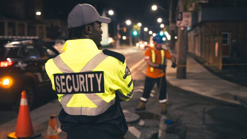 A male Flex Point Security guard standing on-site next to construction workers while they complete their duties