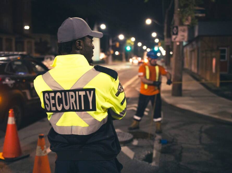 A male Flex Point Security guard standing on-site next to construction workers while they complete their duties