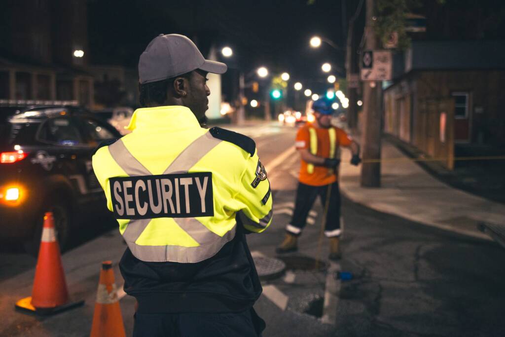 A male Flex Point Security guard standing on-site next to construction workers while they complete their duties