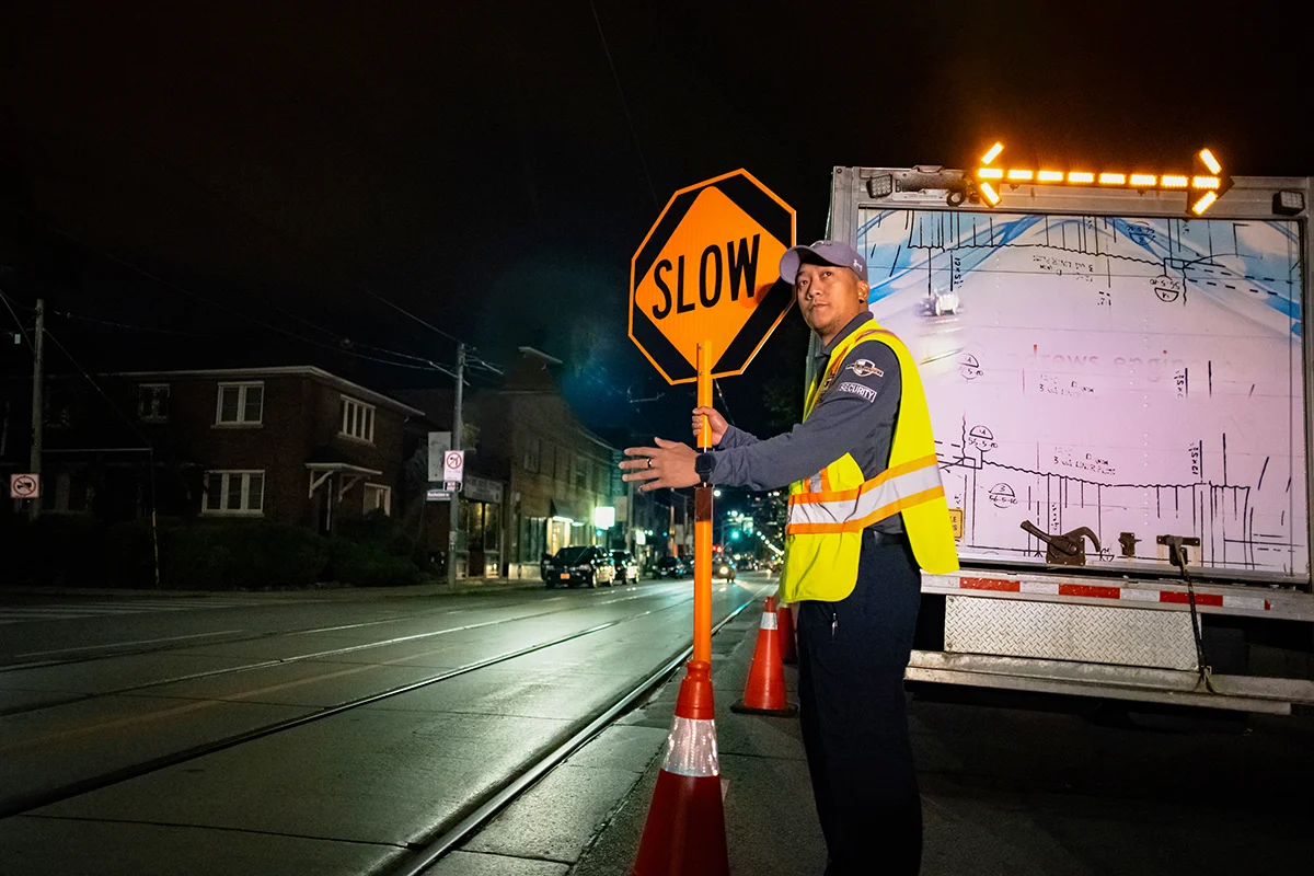 A male Flex Point Security guard on-site at a construction site patrolling traffic with a stop/slow sign