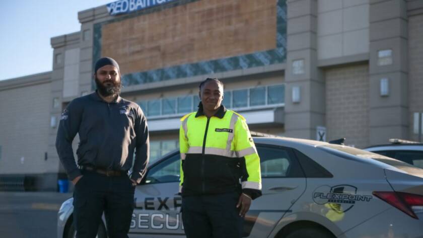 Two Flex Point Security guards standing in front of a company vehicle with a Bed Bath & Beyond behind them