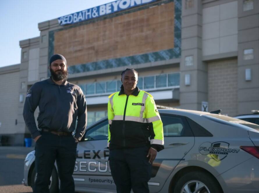 Two Flex Point Security guards standing in front of a company vehicle with a Bed Bath & Beyond behind them