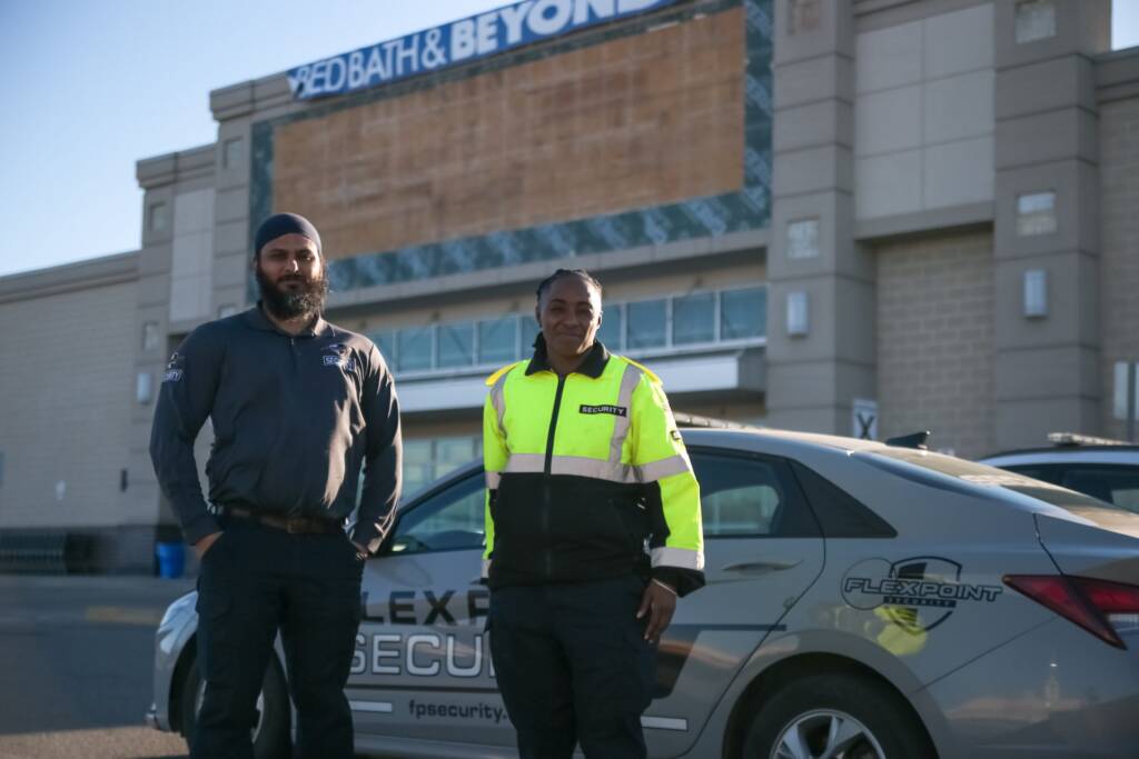Two Flex Point Security guards standing in front of a company vehicle with a Bed Bath & Beyond behind them