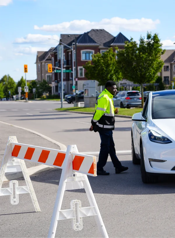 A male Flex Point Security guard standing by a fence to route traffic speaking with a person in a white car