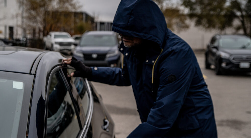 A man wearing a hoodie standing next to a vehicle attempting to break into it